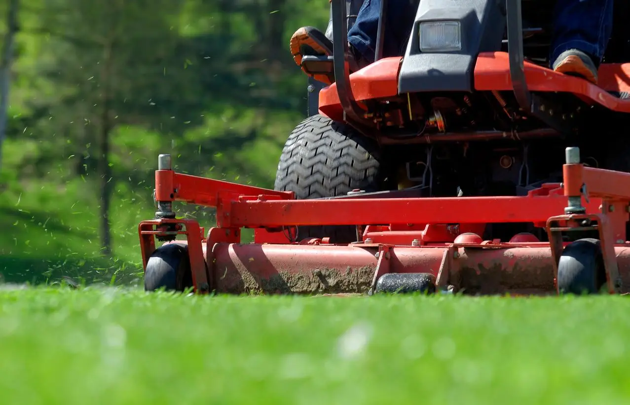 A person on a tractor cutting grass in the yard.