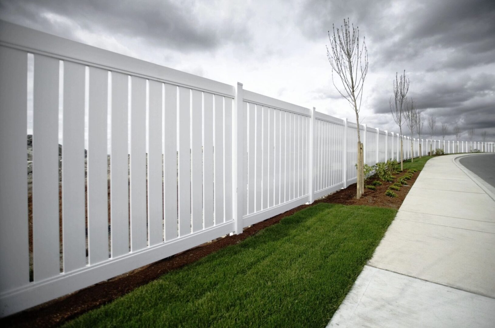 A white fence with grass growing on the side.